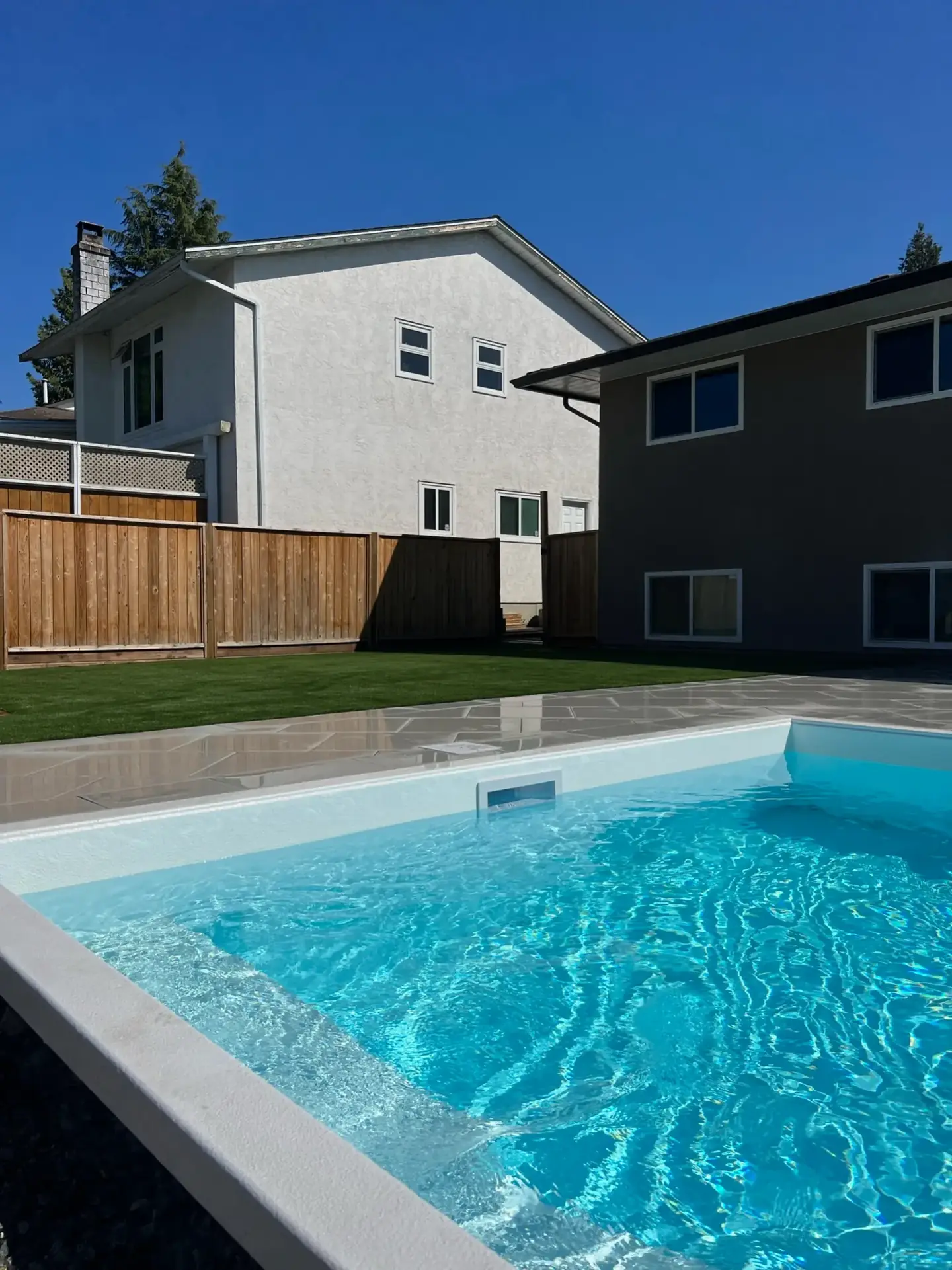 Crystal-clear backyard pool with artificial turf and stone patio surround